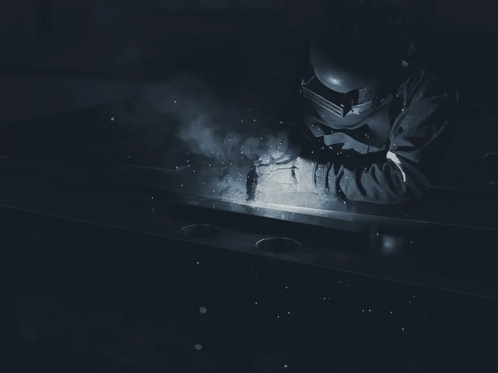 A welder working on metal, sparks lighting a dark workshop